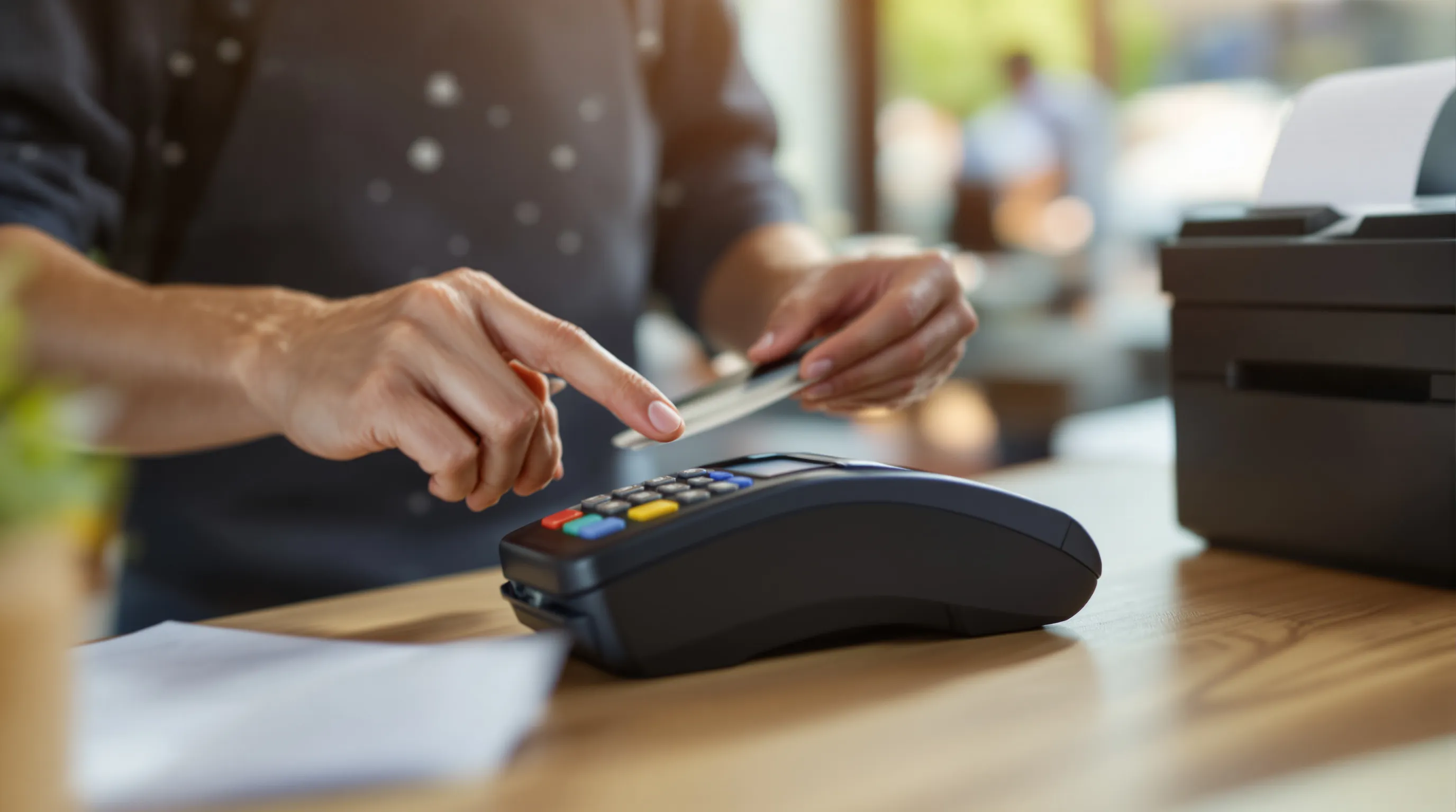 Customer tapping a credit card on a countertop payment terminal while a receipt prints